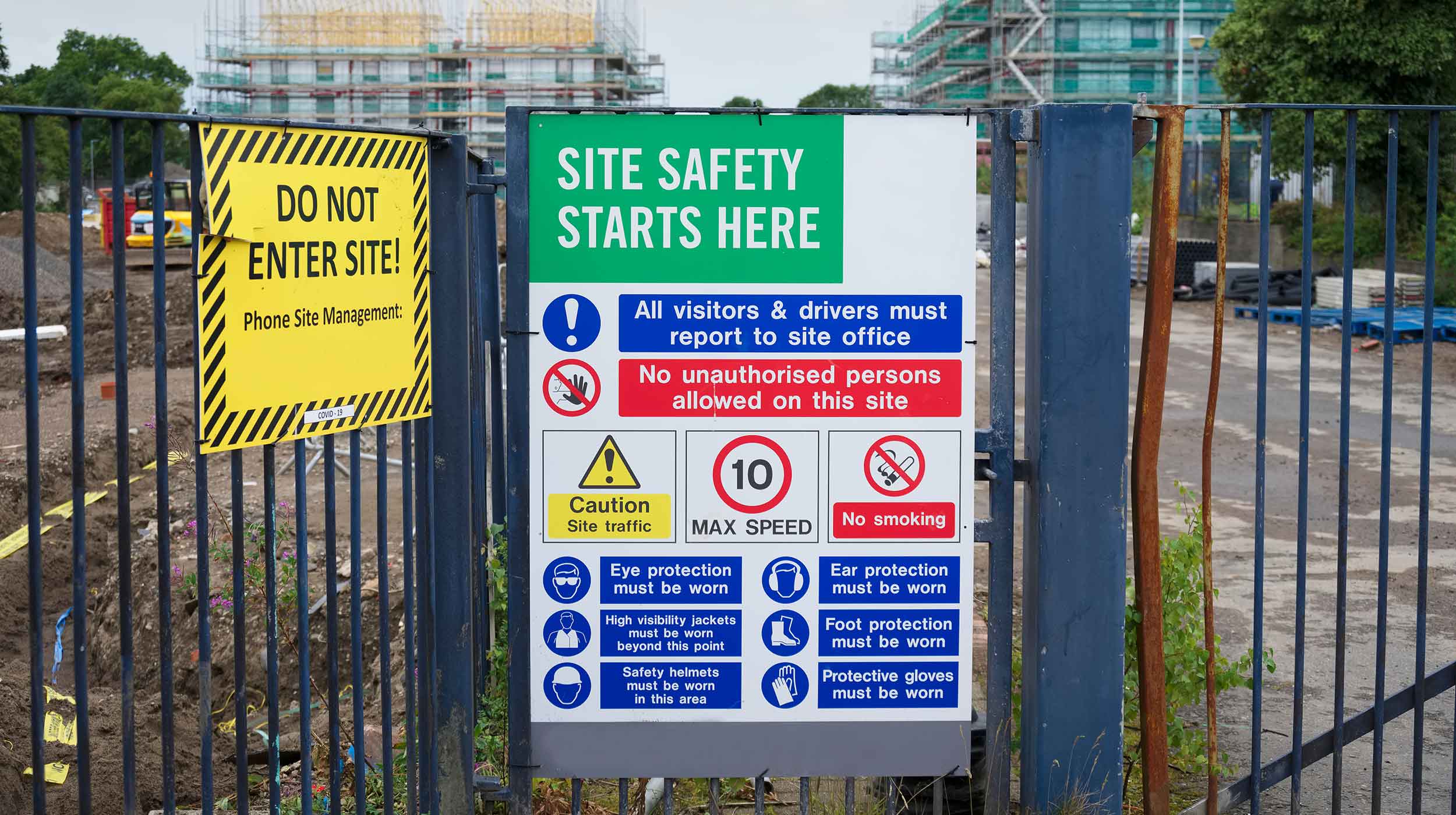 Health and safety signage hanging on a metal fence outside of a job site